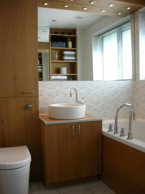 Minimalist bathroom with toilet, sink and bath in view and shelves in the mirror reflection