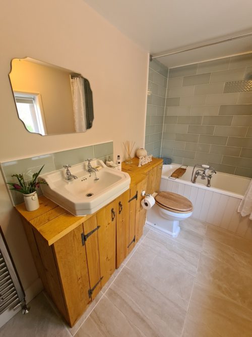 View of bathroom with scaffold board vanity unit, traditional sink, toilet, bath and mirror