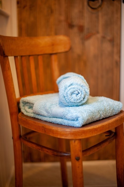 Decorative wooden chair with teal towels in front of cottage door leading onto airing cupboard