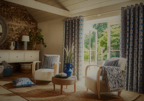 Santorini inspired fabrics set up in living room with French doors open, accent chairs and a coffee table