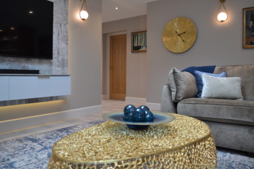 Living room with TV, sofa, rug, gold coffee table, wall lights and gold clock